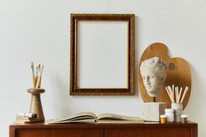 Stylish composition of artist workspace room with design retro teak commode, mock up poster frame, book, decoration and painting accessories. Template. photo