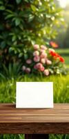 Blank card displayed on a wooden table in a garden with colorful flowers and lush greenery during sunset photo