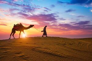 Indian cameleer camel driver camel silhouettes in dunes on sunset. Jaisalmer, Rajasthan, India photo