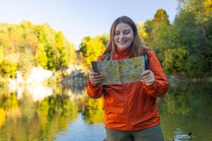 Traveling Happy Caucasian woman with backpack walking on path the mountain forest looking at the camera and map. Summer holiday and vacation trip photo