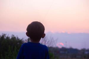 silhouette of a little boy in the field in the afternoon with orange sunlight photo