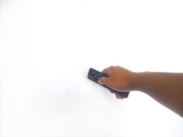 a hand holding a black remote control against a plain white background. The focus is on the remote, highlighting its buttons and ergonomic design. photo