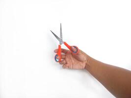 features a hand holding a pair of scissors with orange and blue handles. The scissors appear sharp and ready for use, set against a clean white background that draws attention to the main object. photo