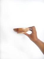 The image shows a hand holding a round wooden bowl with a smooth surface. The plain white background emphasizes the natural texture and grain patterns of the wood, making the bowl the central focus. photo