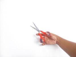 features a hand holding a pair of scissors with orange and blue handles. The scissors appear sharp and ready for use, set against a clean white background that draws attention to the main object. photo