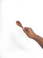 The image shows a hand holding a round wooden spoon with a smooth surface. The plain white background emphasizes the natural texture and grain patterns of the wood, making the bowl the central focus. photo