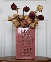 A bouquet of dried roses in a square vase. A motivational saying written on the vase. photo