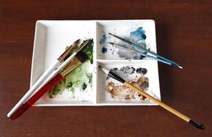 Watercolor paint tray with paint brushes scattered on it. photo