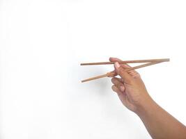 a hand holding a pair of wooden chopsticks against a plain white background. The focus is on the chopsticks, highlighting their smooth texture and natural wooden material. photo