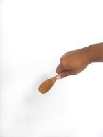 The image shows a hand holding a round wooden spoon with a smooth surface. The plain white background emphasizes the natural texture and grain patterns of the wood, making the bowl the central focus. photo