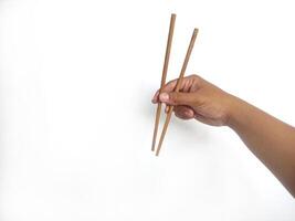 a hand holding a pair of wooden chopsticks against a plain white background. The focus is on the chopsticks, highlighting their smooth texture and natural wooden material. photo