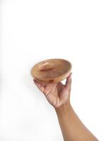 The image shows a hand holding a round wooden bowl with a smooth surface. The plain white background emphasizes the natural texture and grain patterns of the wood, making the bowl the central focus. photo