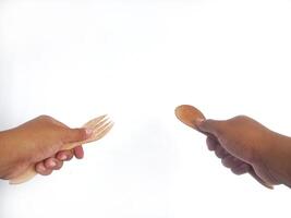 two hands holding wooden utensils one hand holds a wooden fork with three prongs, while the other hand holds a wooden spoon. The utensils showcase a natural wood finish, emphasizing their handcrafted photo
