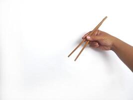 a hand holding a pair of wooden chopsticks against a plain white background. The focus is on the chopsticks, highlighting their smooth texture and natural wooden material. photo