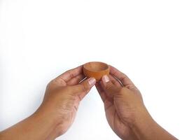 The image shows a pair of hands holding a little round wooden bowl with a smooth surface. The plain white background emphasizes the natural texture and grain patterns of the wood photo