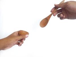 two hands holding a wooden bowl and a wooden spoon. The natural grain of the wood is visible, adding a rustic charm to the image. Set against a clean white background, photo