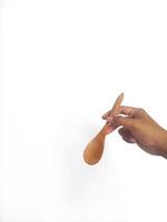 The image shows a hand holding a round wooden spoon with a smooth surface. The plain white background emphasizes the natural texture and grain patterns of the wood, making the bowl the central focus. photo