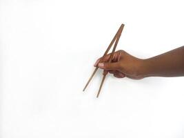 a hand holding a pair of wooden chopsticks against a plain white background. The focus is on the chopsticks, highlighting their smooth texture and natural wooden material. photo
