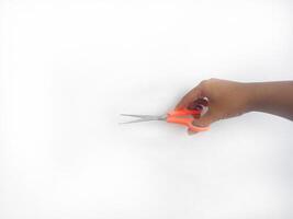 features a hand holding a pair of scissors with orange and blue handles. The scissors appear sharp and ready for use, set against a clean white background that draws attention to the main object. photo