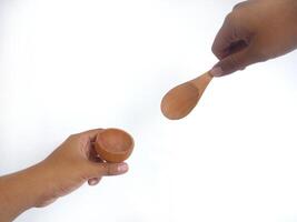two hands holding a wooden bowl and a wooden spoon. The natural grain of the wood is visible, adding a rustic charm to the image. Set against a clean white background, photo