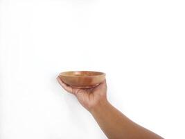 The image shows a hand holding a round wooden bowl with a smooth surface. The plain white background emphasizes the natural texture and grain patterns of the wood, making the bowl the central focus. photo