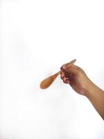 The image shows a hand holding a round wooden spoon with a smooth surface. The plain white background emphasizes the natural texture and grain patterns of the wood, making the bowl the central focus. photo
