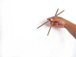 a hand holding a pair of wooden chopsticks against a plain white background. The focus is on the chopsticks, highlighting their smooth texture and natural wooden material. photo