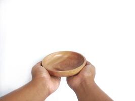 The image shows a pair of hands holding a round wooden bowl with a smooth surface. The plain white background emphasizes the natural texture and grain patterns of the wood, photo