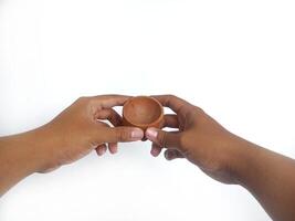 The image shows a pair of hands holding a little round wooden bowl with a smooth surface. The plain white background emphasizes the natural texture and grain patterns of the wood photo