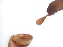 two hands holding a wooden bowl and a wooden spoon. The natural grain of the wood is visible, adding a rustic charm to the image. Set against a clean white background, photo