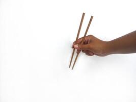a hand holding a pair of wooden chopsticks against a plain white background. The focus is on the chopsticks, highlighting their smooth texture and natural wooden material. photo