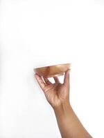 The image shows a hand holding a round wooden bowl with a smooth surface. The plain white background emphasizes the natural texture and grain patterns of the wood, making the bowl the central focus. photo