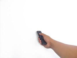 a hand holding a black remote control against a plain white background. The focus is on the remote, highlighting its buttons and ergonomic design. photo
