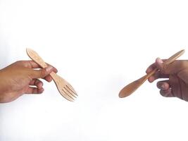 two hands holding wooden utensils one hand holds a wooden fork with three prongs, while the other hand holds a wooden spoon. The utensils showcase a natural wood finish, emphasizing their handcrafted photo