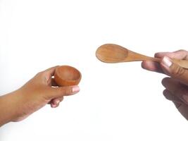 two hands holding a wooden bowl and a wooden spoon. The natural grain of the wood is visible, adding a rustic charm to the image. Set against a clean white background, photo