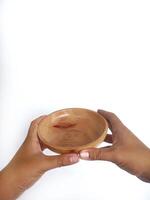 The image shows a pair of hands holding a round wooden bowl with a smooth surface. The plain white background emphasizes the natural texture and grain patterns of the wood, photo