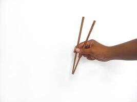 a hand holding a pair of wooden chopsticks against a plain white background. The focus is on the chopsticks, highlighting their smooth texture and natural wooden material. photo