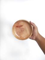 The image shows a hand holding a round wooden bowl with a smooth surface. The plain white background emphasizes the natural texture and grain patterns of the wood, making the bowl the central focus. photo