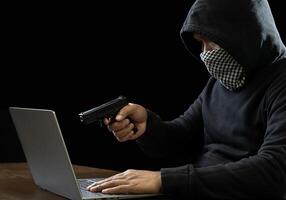 Hacker spy man one person in black hoodie sitting on table looking computer laptop used login password attack security to data digital internet network system night dark background copy space photo