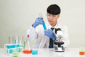 Man asian student education learning scientist wearing doctor gown in lab looking hand at chemist. caused by mixing reagents in scientific research laboratories with test tubes and microscope on table photo