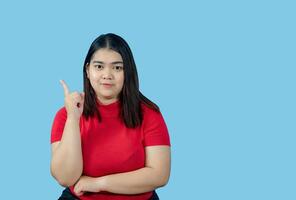 Portrait girl young woman asian chubby fat cute beautiful pretty one person wearing a red shirt is sitting, looking smiling happily holding copyspace imaginary on the isolated blue color background photo