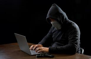 Hacker spy man one person in black hoodie sitting on table looking computer laptop used login password attack security to data digital internet network system night dark background copy space photo