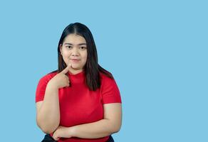 Portrait girl young woman asian chubby fat cute beautiful pretty one person wearing a red shirt is sitting, looking smiling happily holding copyspace imaginary on the isolated blue color background photo