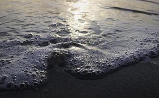 Closeup white bubble sea wave moving ,blurred Sea beach in morning time,reflection of sunrise shining around, photo