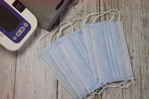 Surgical Mask put beside blood pressure monitor on wood background photo
