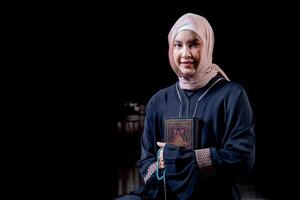 The image of an Asian Muslim woman in the Islamic religion in hijab in cream color. reading the Quran and having a happy smiling face Staying in a beautiful mosque out of respect for God. photo