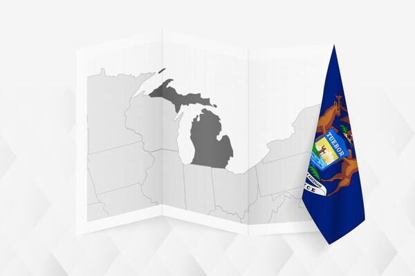 A grayscale map of Michigan with a hanging Michigan flag on one side. Map for many types of news.