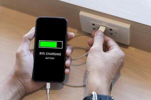 Man hand holding smart phone and charging battery from built in usb socket on the table. photo