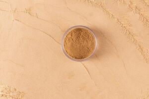 A round transparent jar with loose powder in bronze tone stands on a large sample of powder in a natural tone. top view. texture. A copy space. photo