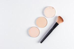 Three round blocks, a refill of compact powder in various tones, lie diagonally on a white background with a beautiful makeup brush. top view. space. photo